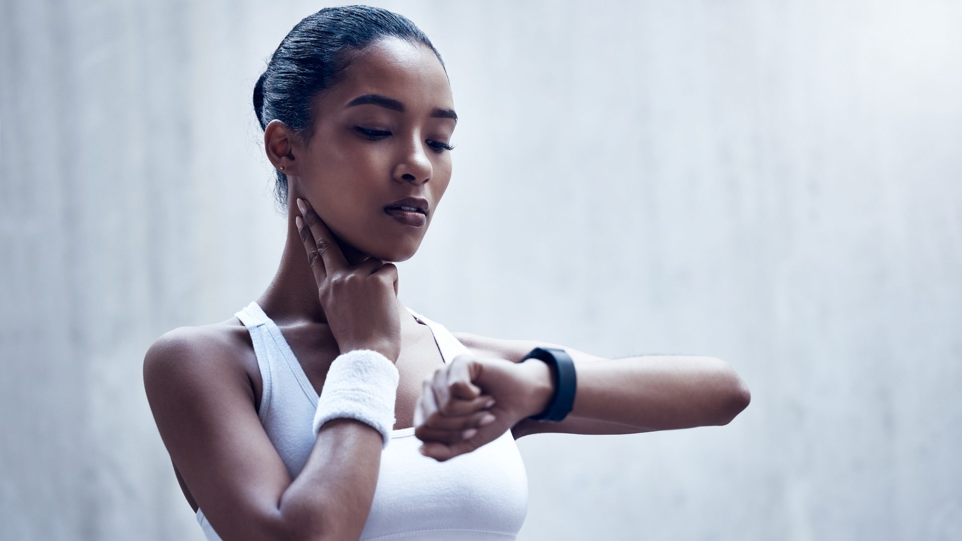 Woman with a wristband on her wrist and a hand on her neck checking her heart rate